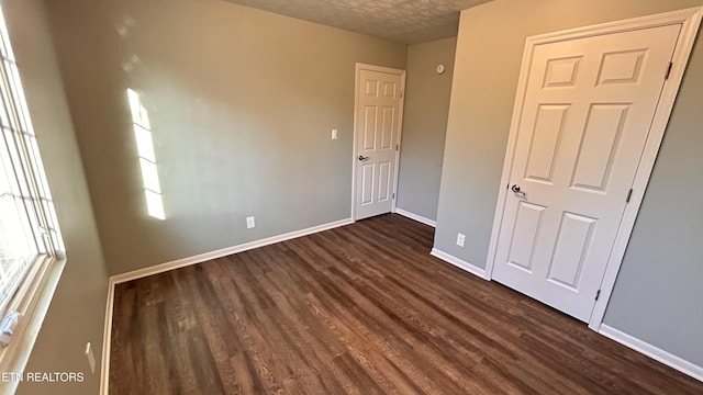 unfurnished bedroom featuring baseboards, a textured ceiling, and dark wood-style flooring