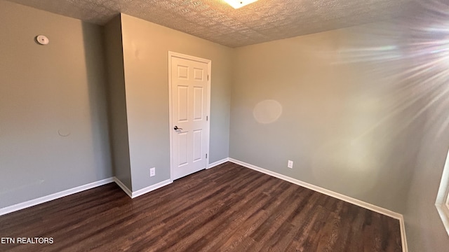 empty room with a textured ceiling, dark wood-type flooring, and baseboards