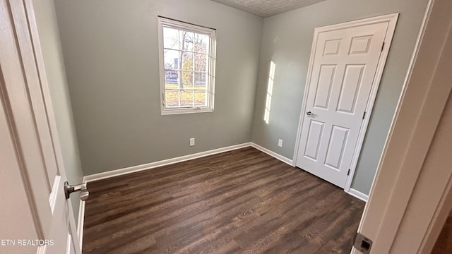 unfurnished bedroom featuring baseboards, a textured ceiling, and dark wood finished floors