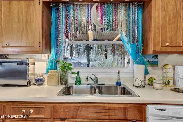 kitchen featuring white dishwasher, light countertops, brown cabinets, and a sink