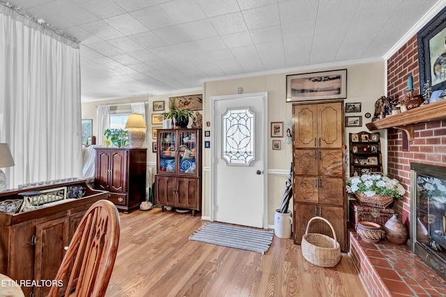 foyer featuring light wood-style flooring, a brick fireplace, and ornamental molding