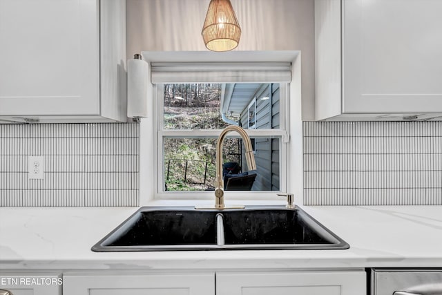 interior details with a sink, light stone counters, dishwasher, and white cabinets