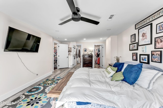 bedroom featuring wood finished floors, visible vents, baseboards, recessed lighting, and a walk in closet