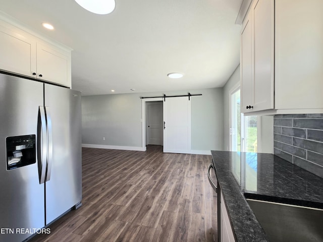 kitchen with dark wood finished floors, dark stone counters, stainless steel fridge with ice dispenser, a barn door, and tasteful backsplash