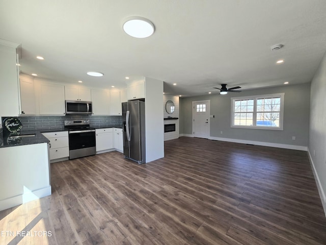 kitchen with dark countertops, backsplash, open floor plan, appliances with stainless steel finishes, and dark wood-style floors