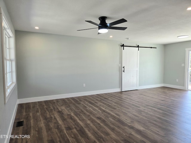 empty room featuring a barn door, baseboards, and dark wood-type flooring