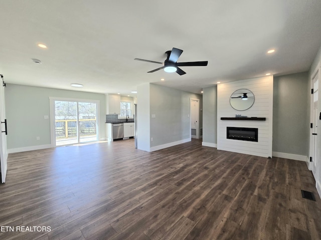 unfurnished living room with visible vents, a ceiling fan, dark wood-style floors, a barn door, and a large fireplace