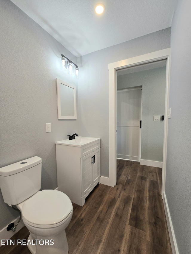 half bath featuring baseboards, toilet, wood finished floors, a textured wall, and vanity