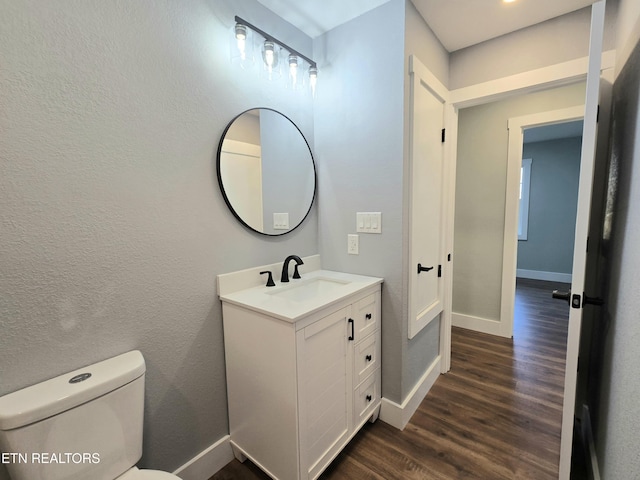 bathroom featuring baseboards, toilet, wood finished floors, a textured wall, and vanity