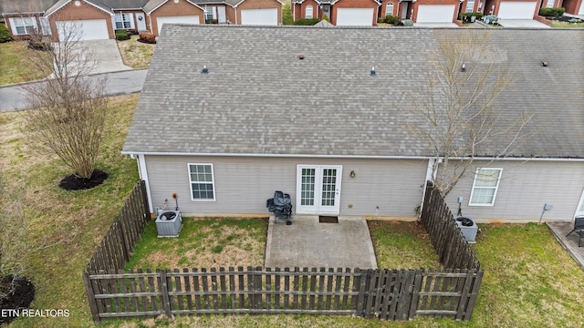 rear view of property featuring a lawn, french doors, a shingled roof, and a fenced backyard