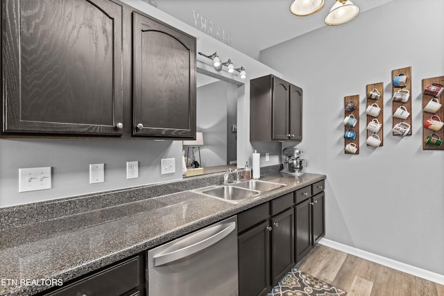 kitchen featuring dark countertops, baseboards, light wood-type flooring, stainless steel dishwasher, and a sink