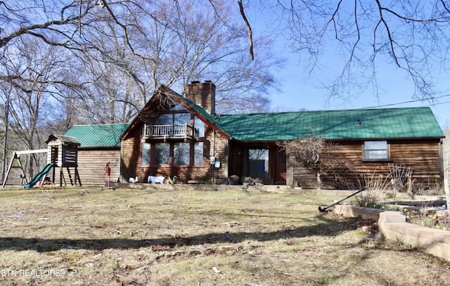 back of house featuring metal roof, a balcony, a chimney, and a playground