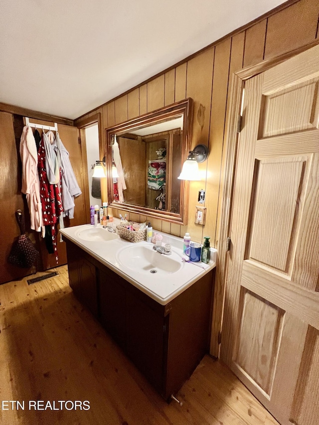 bathroom with a sink, wood finished floors, double vanity, and wood walls