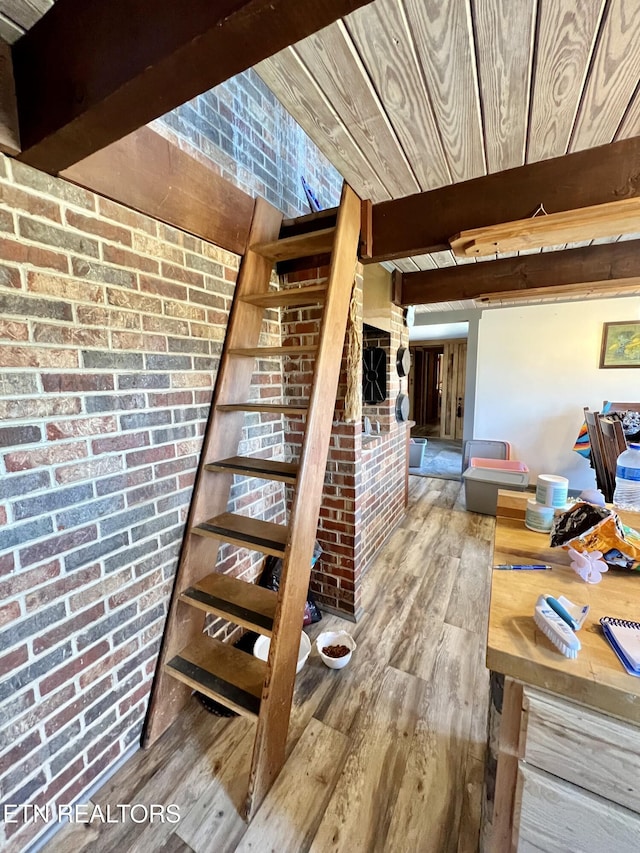 stairway featuring wood finished floors, beamed ceiling, wood ceiling, and brick wall