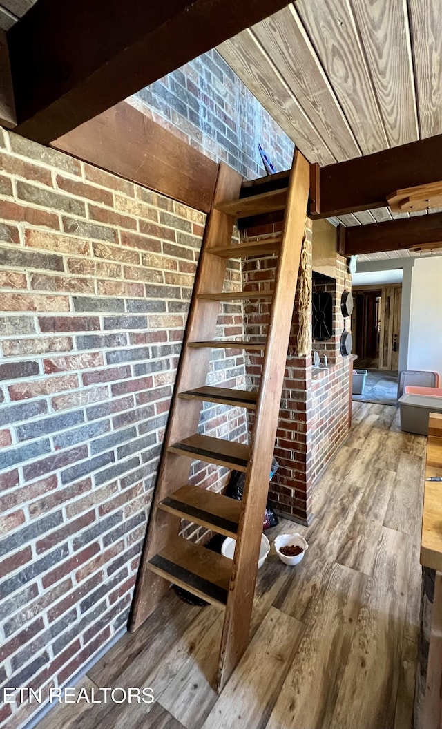 stairway featuring beamed ceiling, brick wall, wood ceiling, and wood finished floors