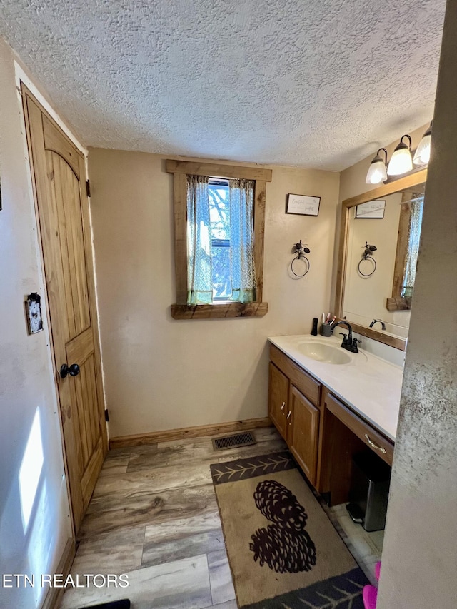 bathroom with visible vents, a textured ceiling, wood finished floors, baseboards, and vanity