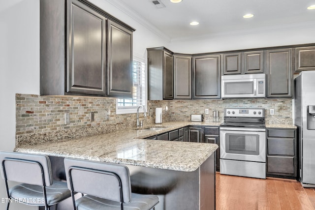 kitchen with light wood-style flooring, ornamental molding, a sink, a peninsula, and appliances with stainless steel finishes