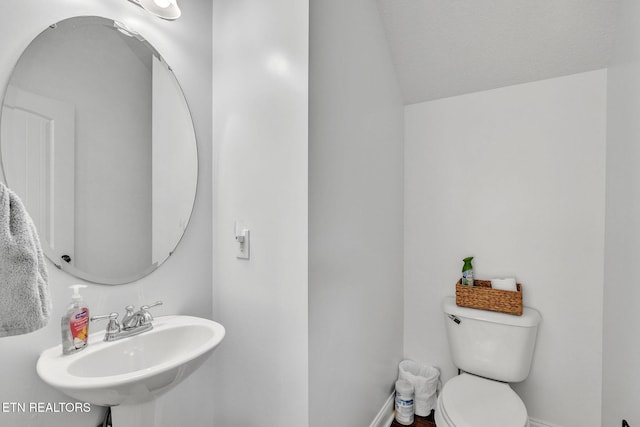 bathroom with lofted ceiling, toilet, baseboards, and a sink