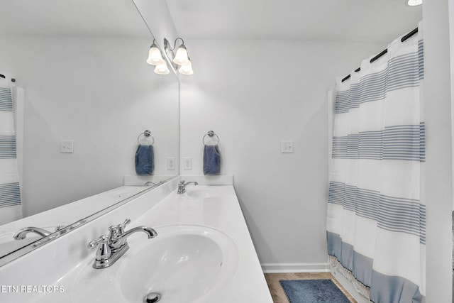 bathroom with double vanity, a shower with shower curtain, baseboards, and a sink