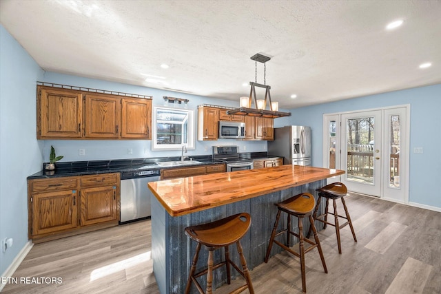 kitchen with a breakfast bar area, brown cabinets, appliances with stainless steel finishes, wood counters, and a sink