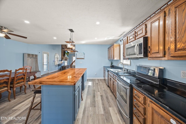 kitchen with a center island, a sink, stainless steel appliances, light wood-style floors, and butcher block counters