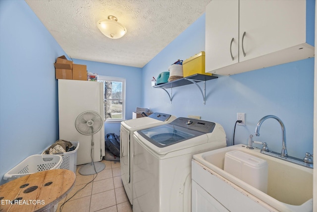 washroom featuring a sink, a textured ceiling, washing machine and dryer, cabinet space, and light tile patterned floors