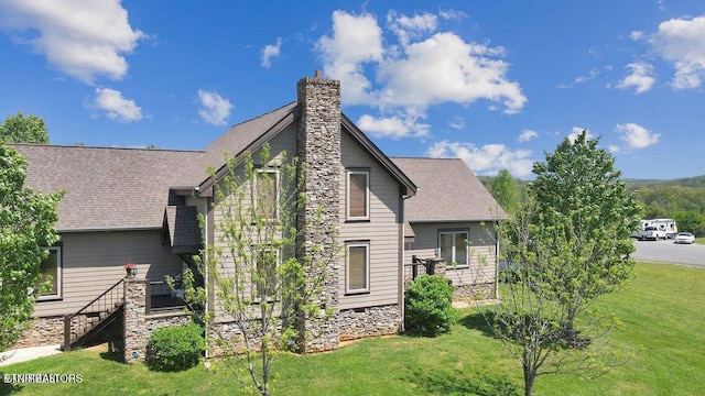 view of side of home with a lawn, a chimney, and a shingled roof