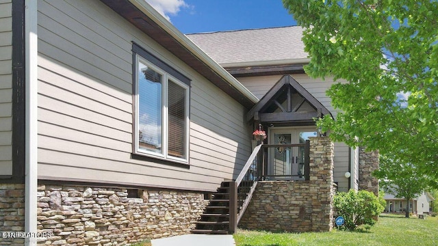 doorway to property with stone siding and a shingled roof