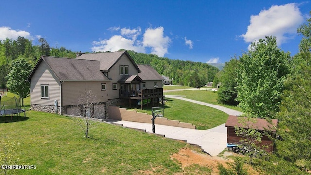 view of property exterior featuring a deck, a trampoline, a yard, and a shingled roof