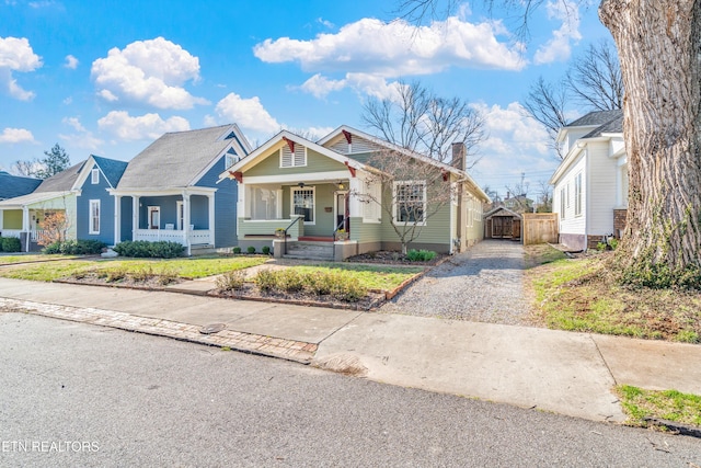 bungalow-style home with covered porch, driveway, a chimney, and a gate