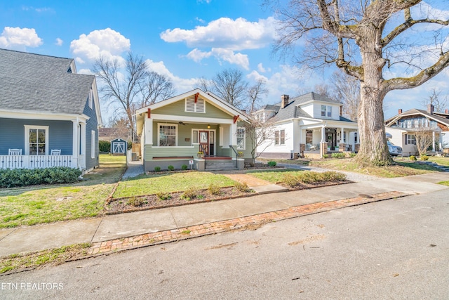 bungalow-style house with a storage shed, a porch, a front lawn, and an outdoor structure