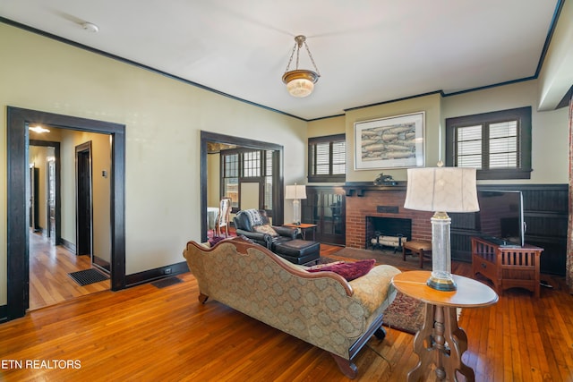 living area featuring baseboards, wood-type flooring, ornamental molding, and a fireplace