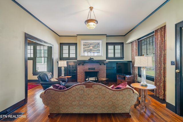 living area with baseboards, wood finished floors, a fireplace, and crown molding