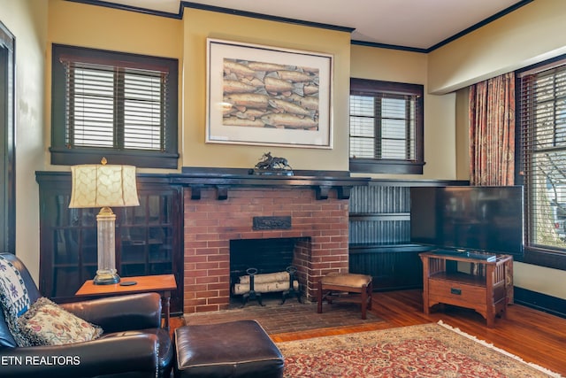 living room with wood finished floors, plenty of natural light, a brick fireplace, and ornamental molding