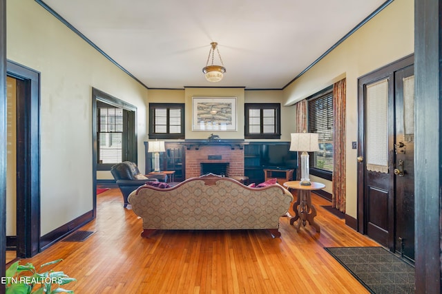 living area featuring visible vents, ornamental molding, wood finished floors, baseboards, and a brick fireplace