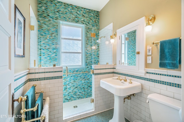 bathroom with a wainscoted wall, tile walls, toilet, and a stall shower