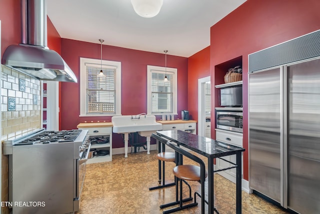 kitchen with premium appliances, backsplash, ventilation hood, baseboards, and hanging light fixtures