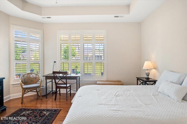 bedroom with visible vents, a raised ceiling, baseboards, and wood finished floors