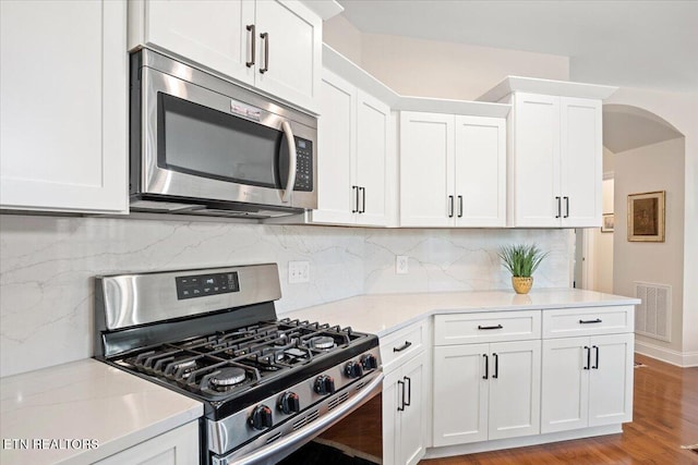 kitchen featuring light wood finished floors, visible vents, appliances with stainless steel finishes, arched walkways, and white cabinets