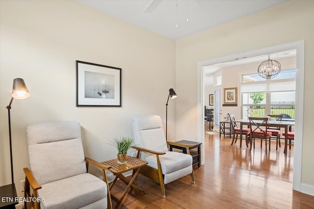 living area with ceiling fan with notable chandelier, wood finished floors, and baseboards