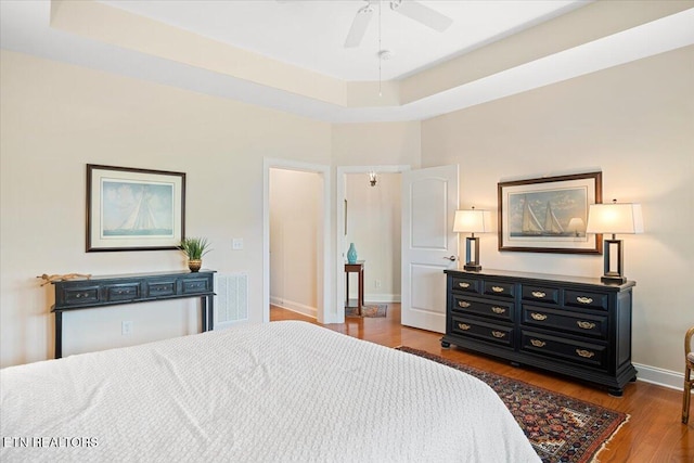 bedroom featuring visible vents, ceiling fan, baseboards, a tray ceiling, and wood finished floors