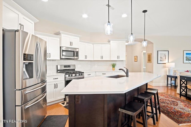 kitchen with a sink, light countertops, appliances with stainless steel finishes, a kitchen bar, and tasteful backsplash