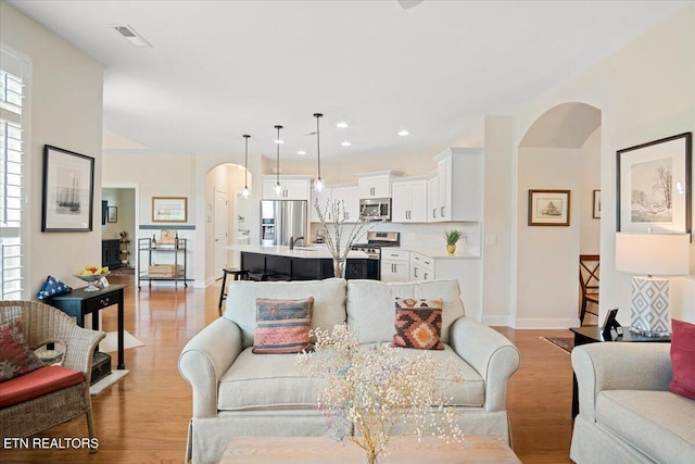 living room featuring arched walkways, a healthy amount of sunlight, and light wood-style flooring