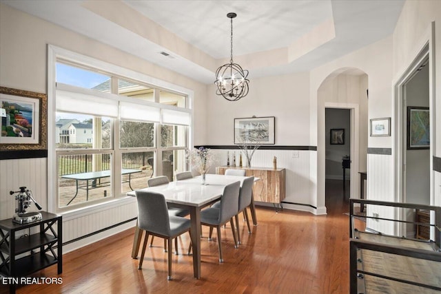 dining space featuring visible vents, a wainscoted wall, wood finished floors, arched walkways, and a raised ceiling