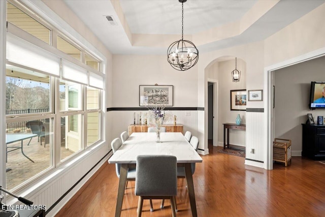 dining space with visible vents, hardwood / wood-style flooring, a tray ceiling, arched walkways, and an inviting chandelier