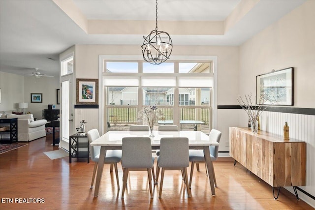 dining room featuring a tray ceiling, a notable chandelier, and light wood-style flooring