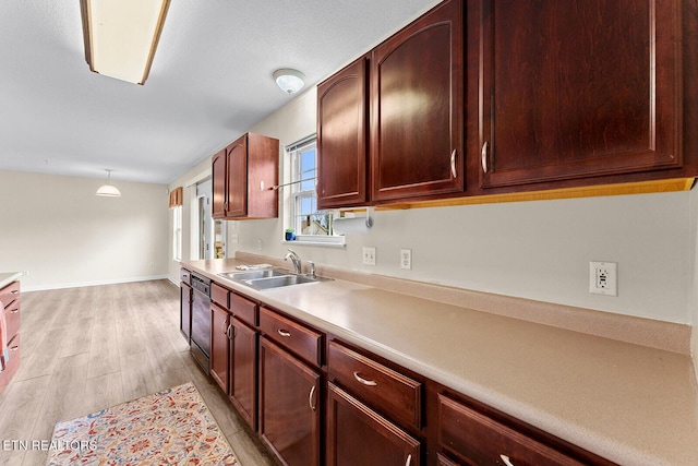 kitchen featuring light wood-style flooring, a sink, decorative light fixtures, light countertops, and dishwashing machine