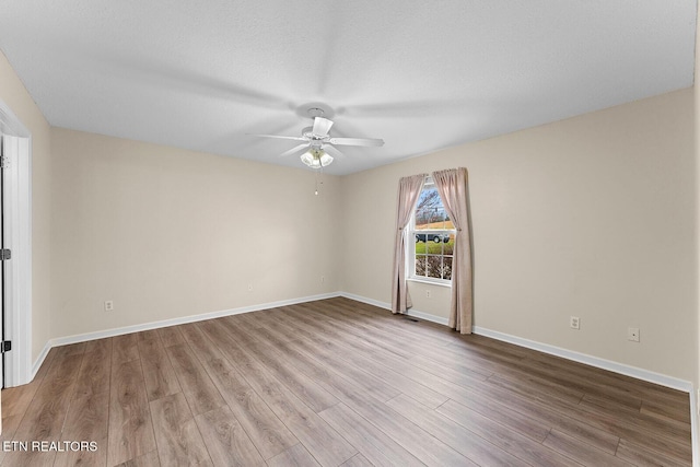 unfurnished room featuring baseboards, wood finished floors, and ceiling fan