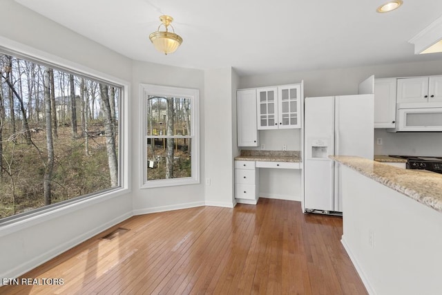 kitchen with hardwood / wood-style floors, white appliances, built in study area, glass insert cabinets, and white cabinetry