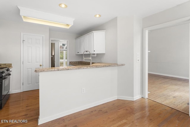 kitchen with light wood finished floors, light stone counters, a wood stove, white cabinetry, and black / electric stove